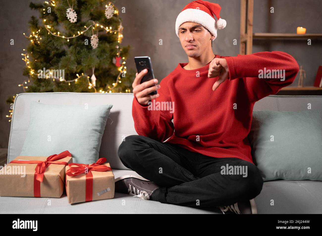 J'ai déçu l'homme arabe dans le chapeau de santa montrant le pouce vers le bas geste à l'aide de l'application mobile de téléphone de livraison. Mauvais examen et service de livraison de cadeau en ligne pour Christma Banque D'Images