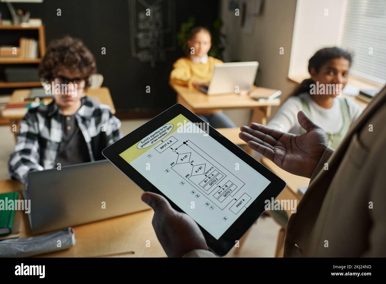 Gros plan d'un professeur afro-américain utilisant une tablette numérique avec des graphiques à l'écran et parlant aux enfants en cours Banque D'Images