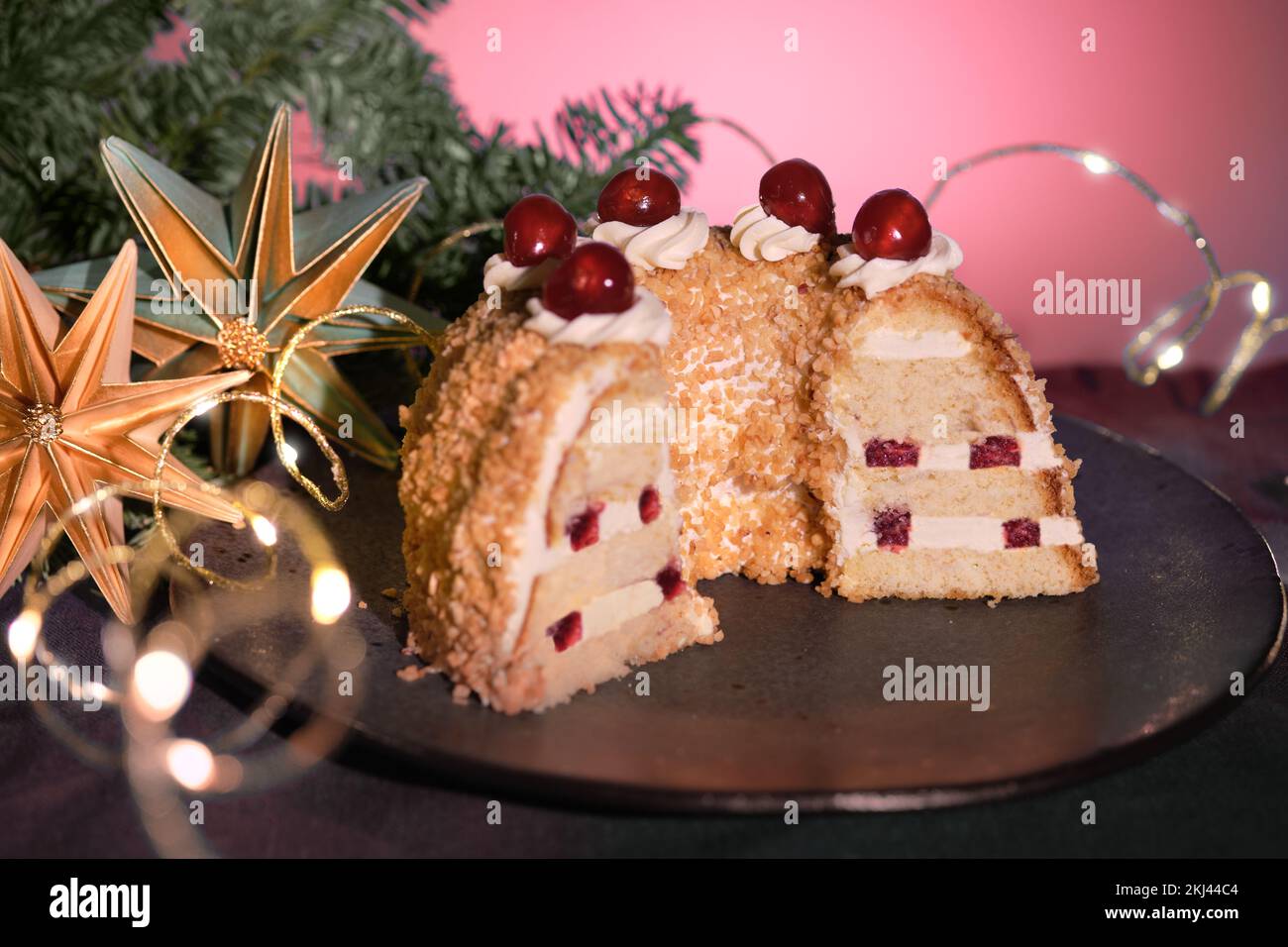 Gâteau allemand Frankfurter Kranz ou Frankfurt Crown Cake. Bisquit à la crème de beurre, cerise. La moitié du gâteau sur une assiette noire. Arrière-plan noir et rose Banque D'Images