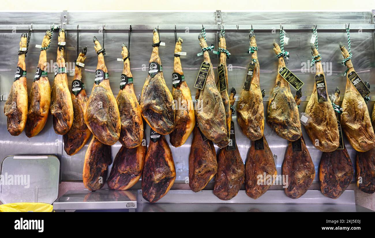 Alicante, Espagne - 12 septembre 2022: Plusieurs pattes de jambon Serrano fumé en vente dans un grand magasin. Les jambons sont attachés avec des cordes et accrochés à un po Banque D'Images