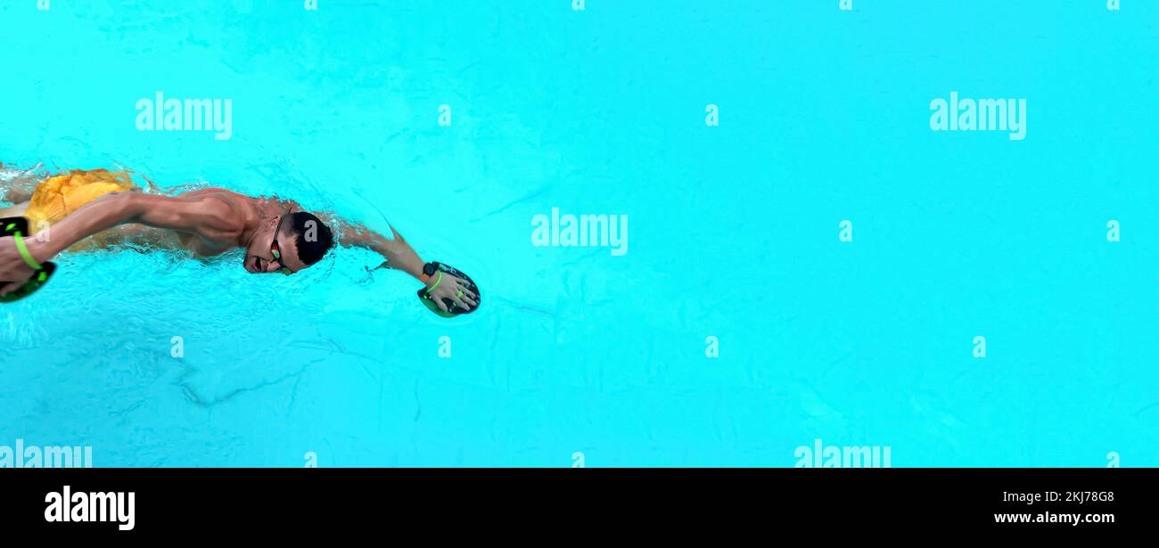 Des trains d'homme dans la piscine. Vue d'en haut sur un nageur ailetique homme nageant dans l'eau claire bleue portant des lunettes pour nager et utiliser des palettes à main Banque D'Images