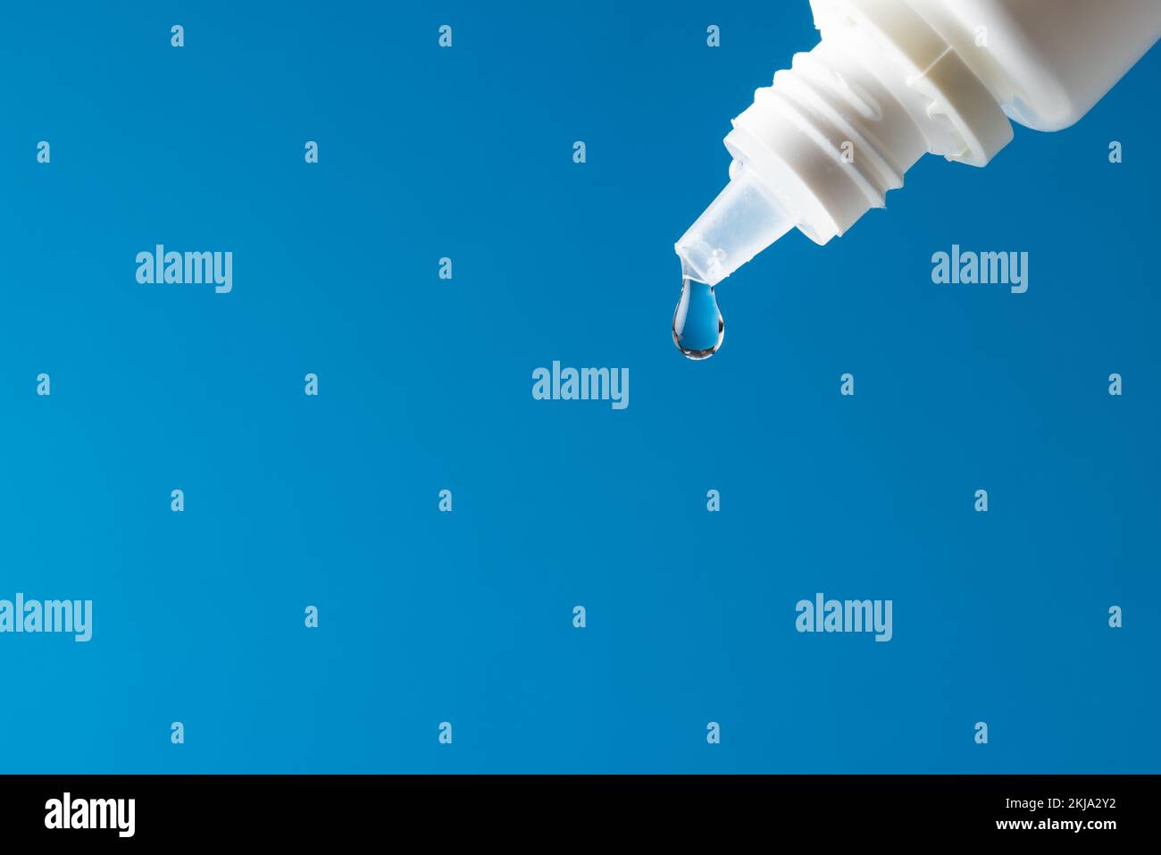 Composition de la goutte tombant de la bouteille compte-gouttes blanche sur fond bleu avec espace de copie Banque D'Images