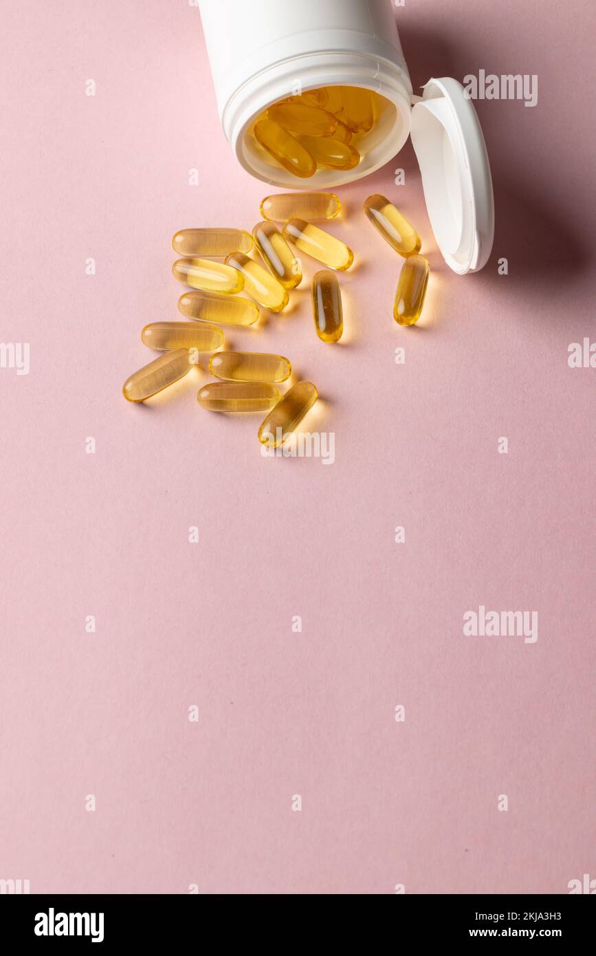 Composition verticale de la boîte de pilules blanche qui déborde les capsules d'huile sur fond rose avec espace de copie Banque D'Images