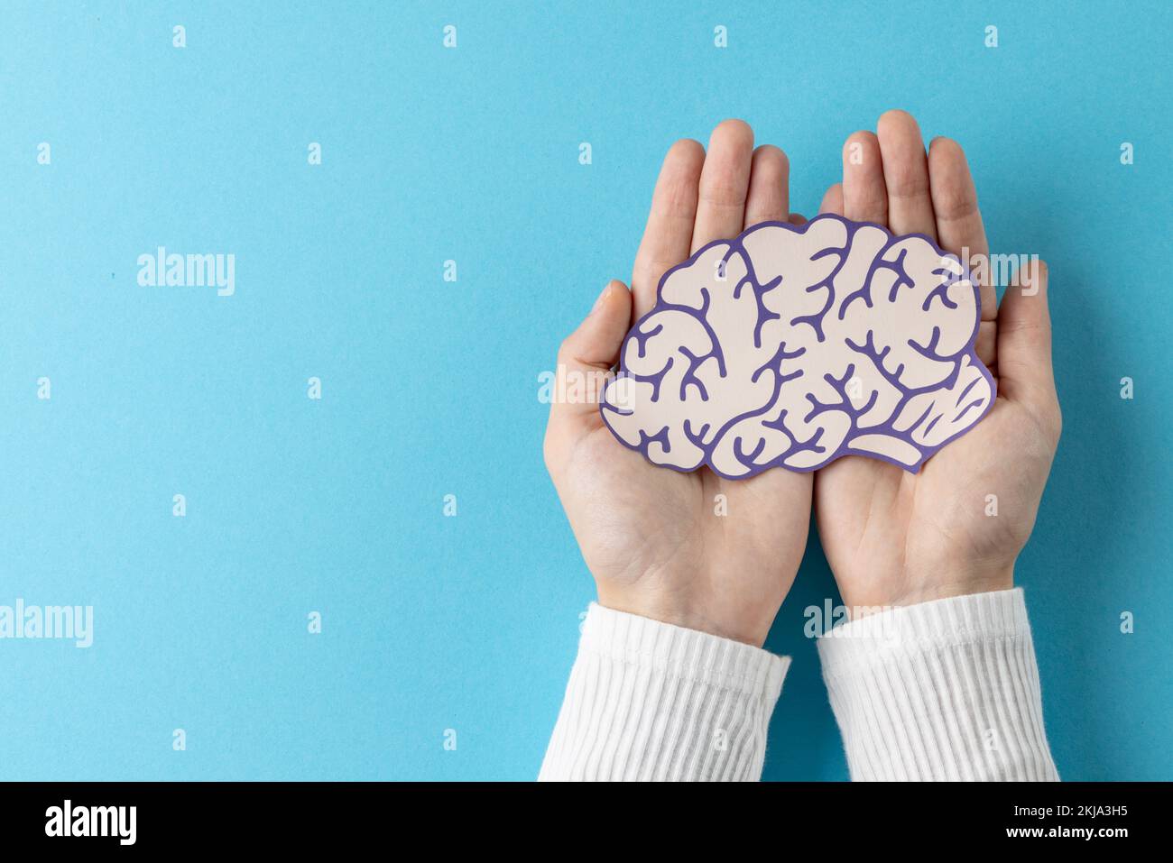 Composition des mains tenant le cerveau violet et blanc sur fond bleu avec espace de copie Banque D'Images