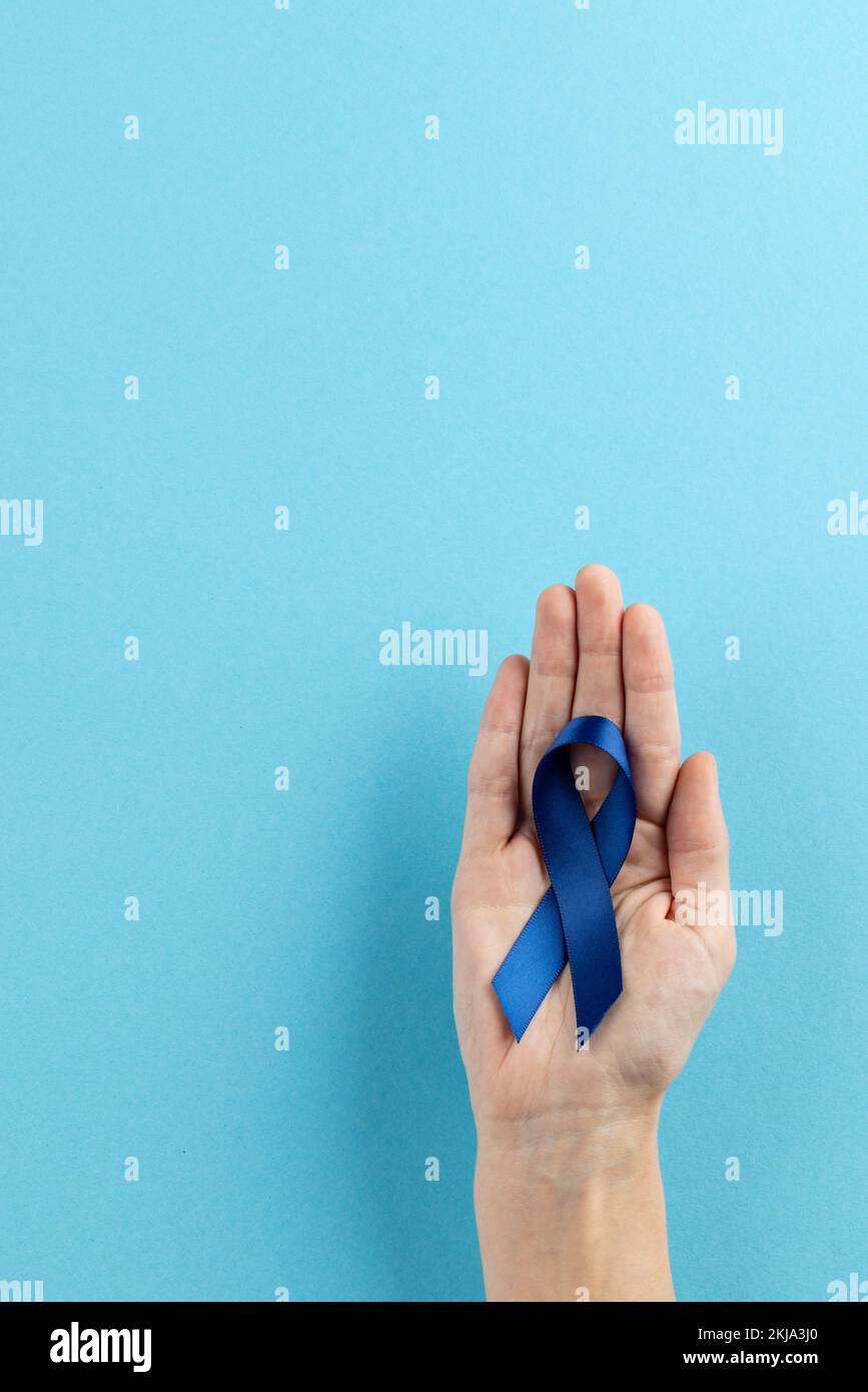 Vertical de la main tenant bleu ruban de sensibilisation au cancer du côlon sur fond bleu avec espace de copie Banque D'Images