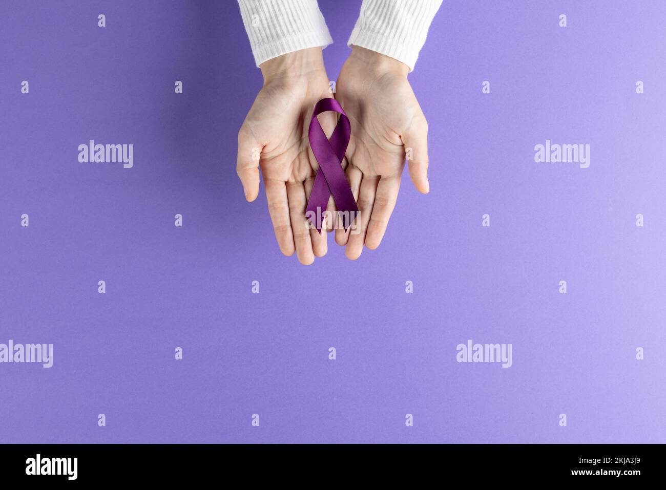 Mains tenant ruban de sensibilisation au cancer du pancréas violet sur fond violet avec espace de copie Banque D'Images