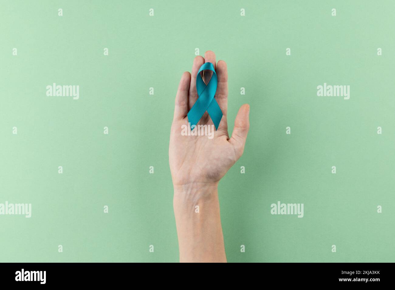 Composition de la main tenant bleu ruban de sensibilisation au cancer de l'ovaire sur fond vert avec espace de copie Banque D'Images