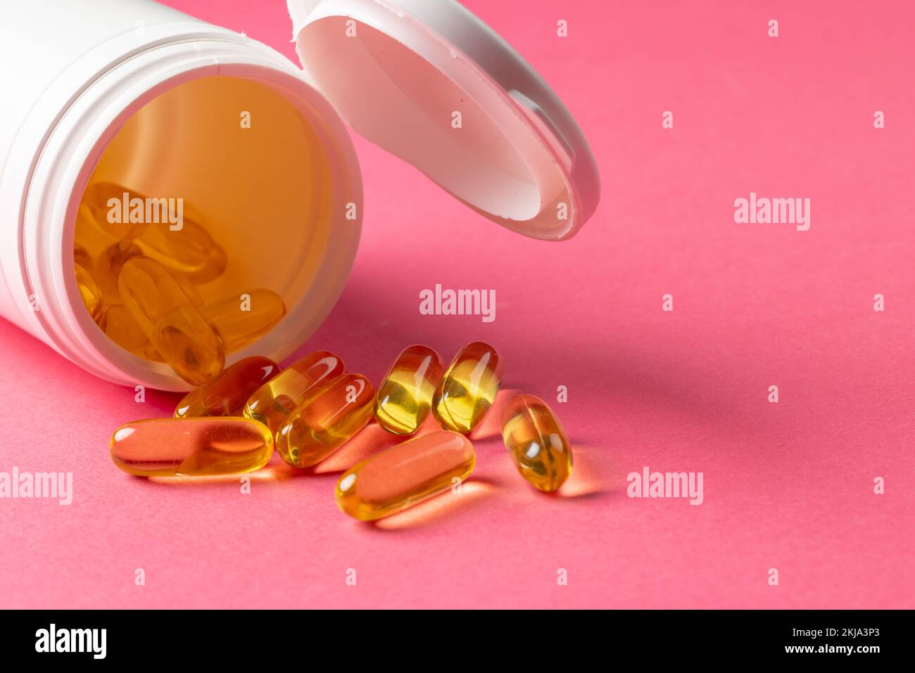 Composition d'une bouteille de pilules blanches qui déborde de capsules d'huile sur fond rose avec espace de copie Banque D'Images