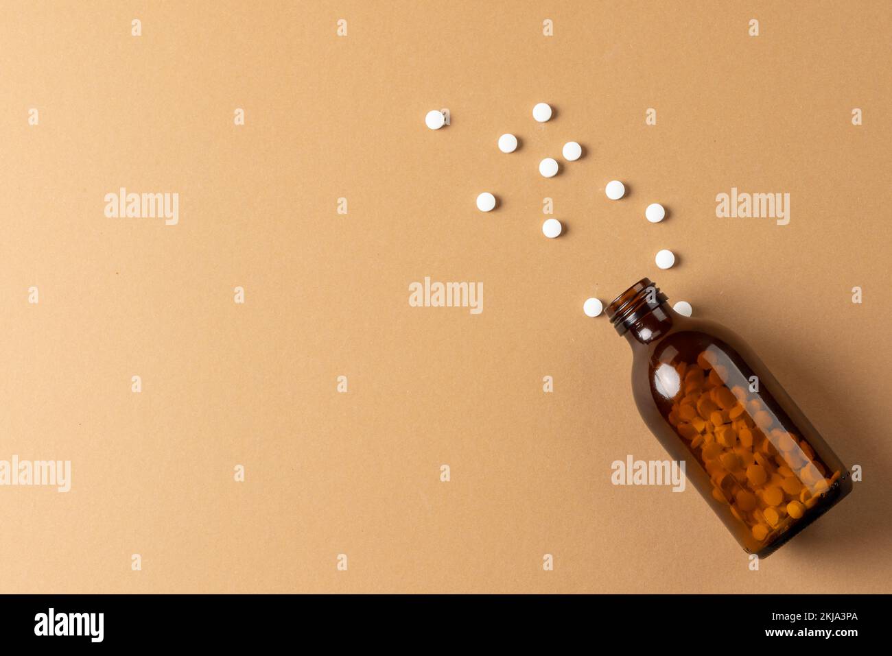 Composition d'un flacon de pilule en verre brun qui déborde de pilules blanches sur fond marron avec espace de copie Banque D'Images