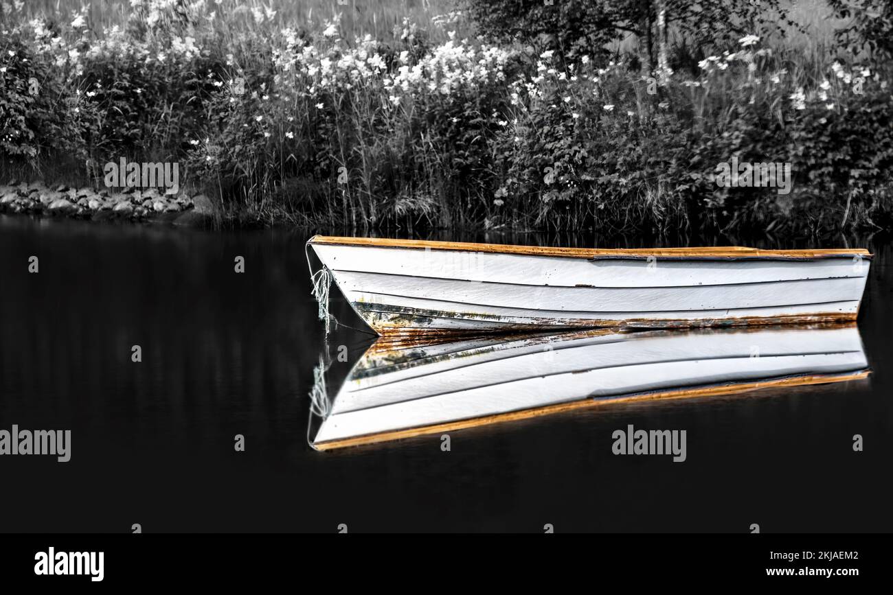 Une image en noir et blanc avec une touche de couleur d'un bateau et son reflet sur l'eau, l'atmosphère sombre et sinistre, l'aspect vintage, horizontal Banque D'Images