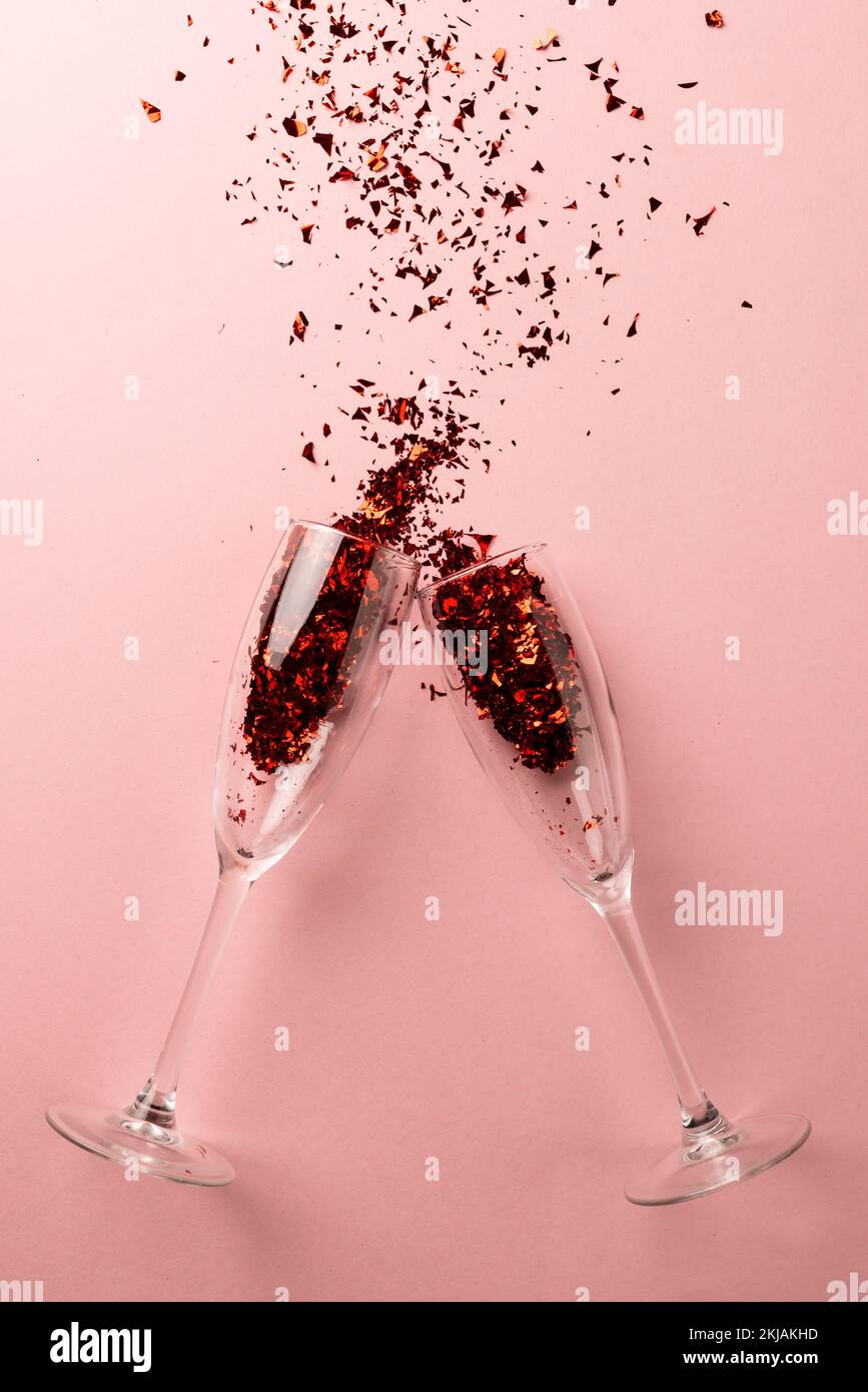 Verticale de deux verres à champagne qui débordent de confettis rouges scintillants sur fond rose pâle Banque D'Images