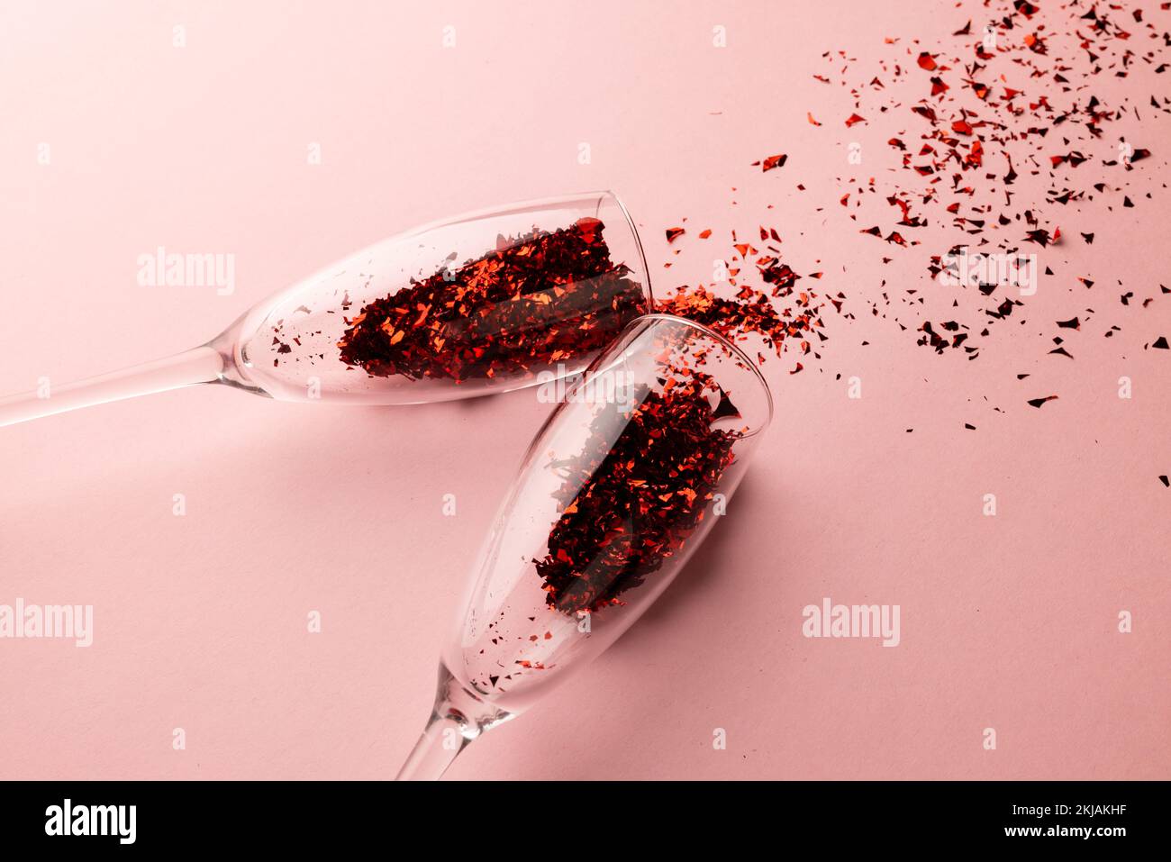 Deux verres à champagne renversant des confettis rouges scintillants sur fond rose pâle avec espace pour les copies Banque D'Images