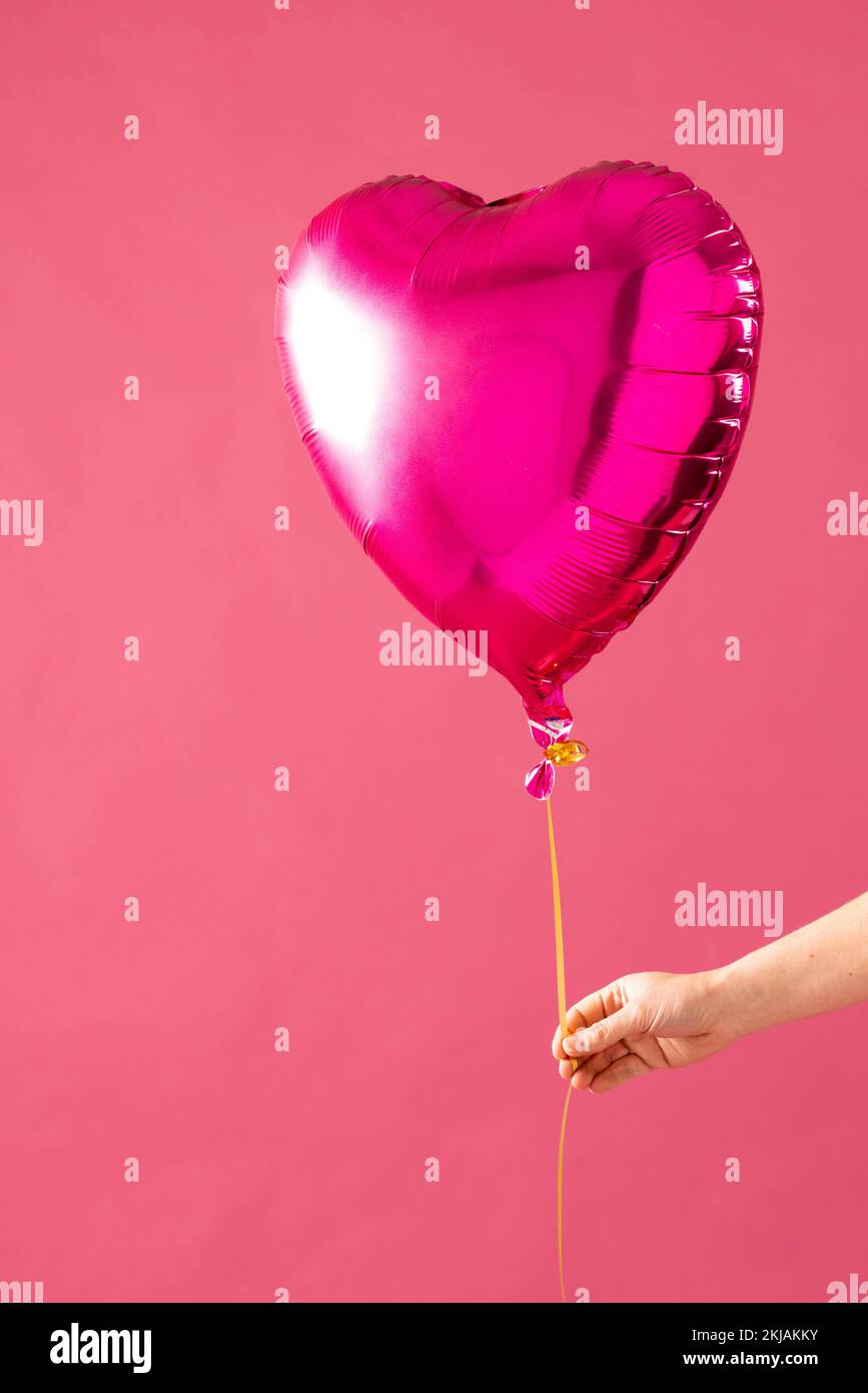 Vertical de la main tenant un ballon rose brillant en forme de coeur sur fond rose avec espace de copie Banque D'Images