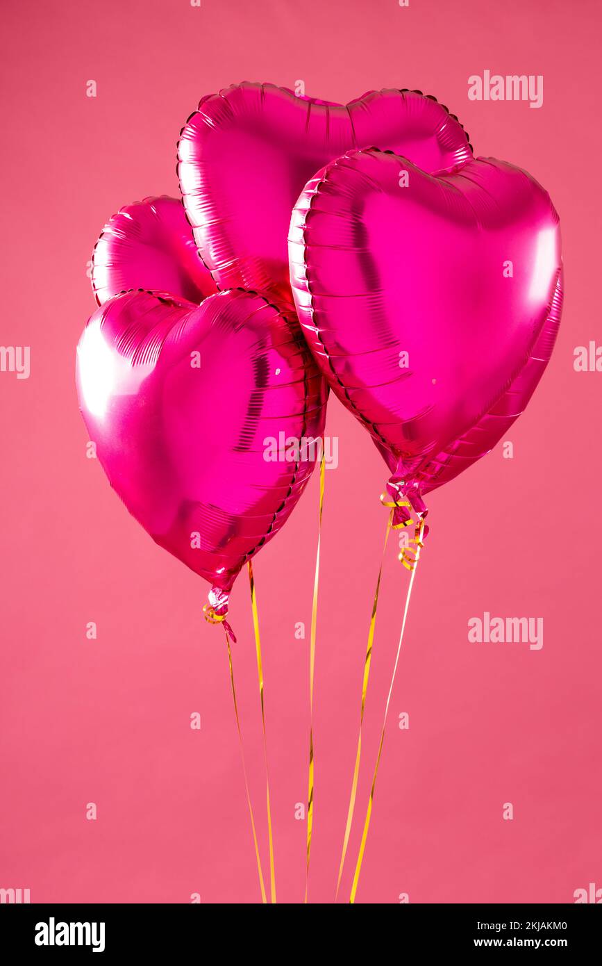 Verticale de quatre ballons en forme de coeur rose brillant flottant sur fond blanc avec espace de copie Banque D'Images