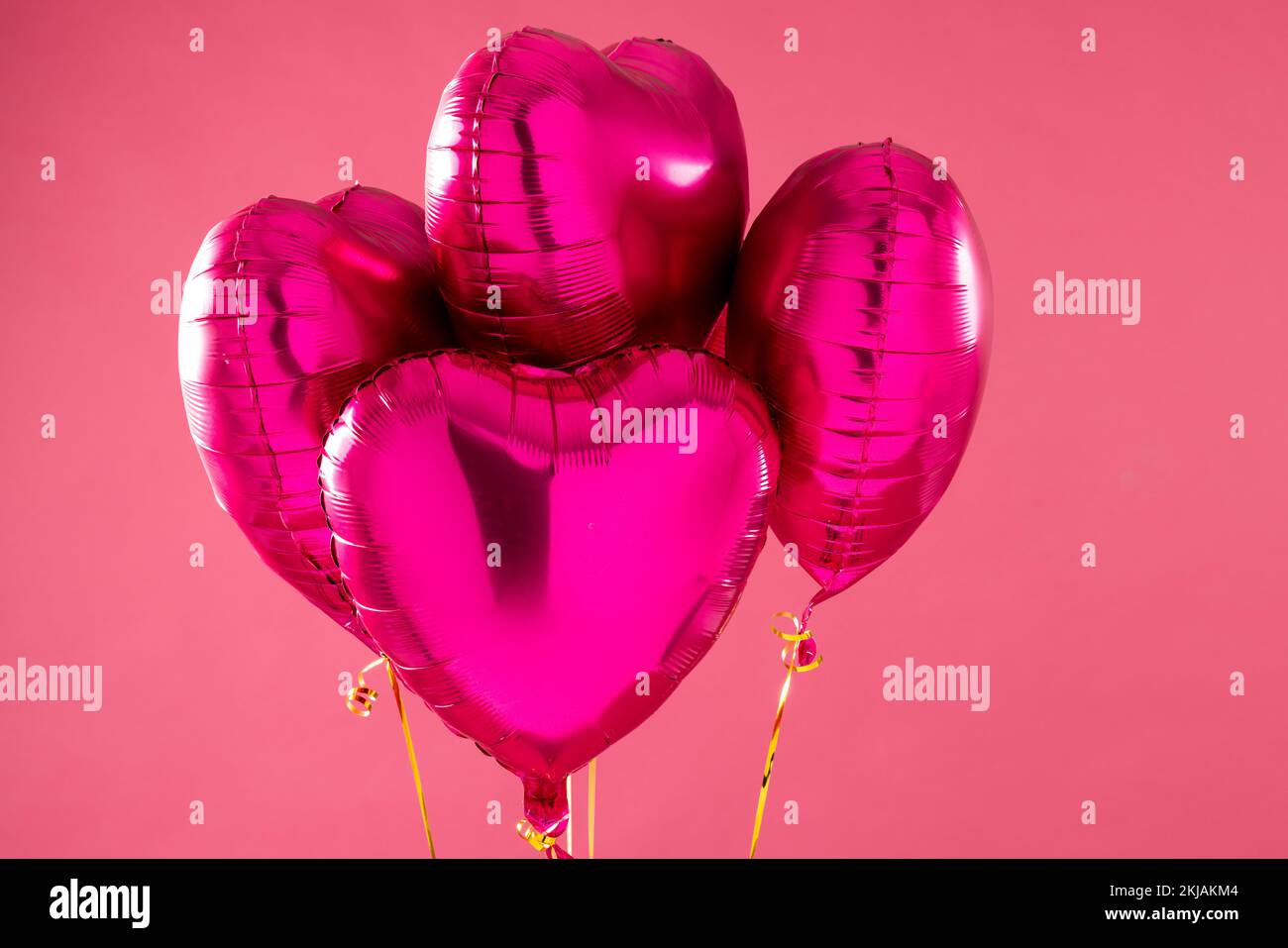 Quatre ballons en forme de coeur rose brillant flottant sur fond rose avec espace de copie Banque D'Images