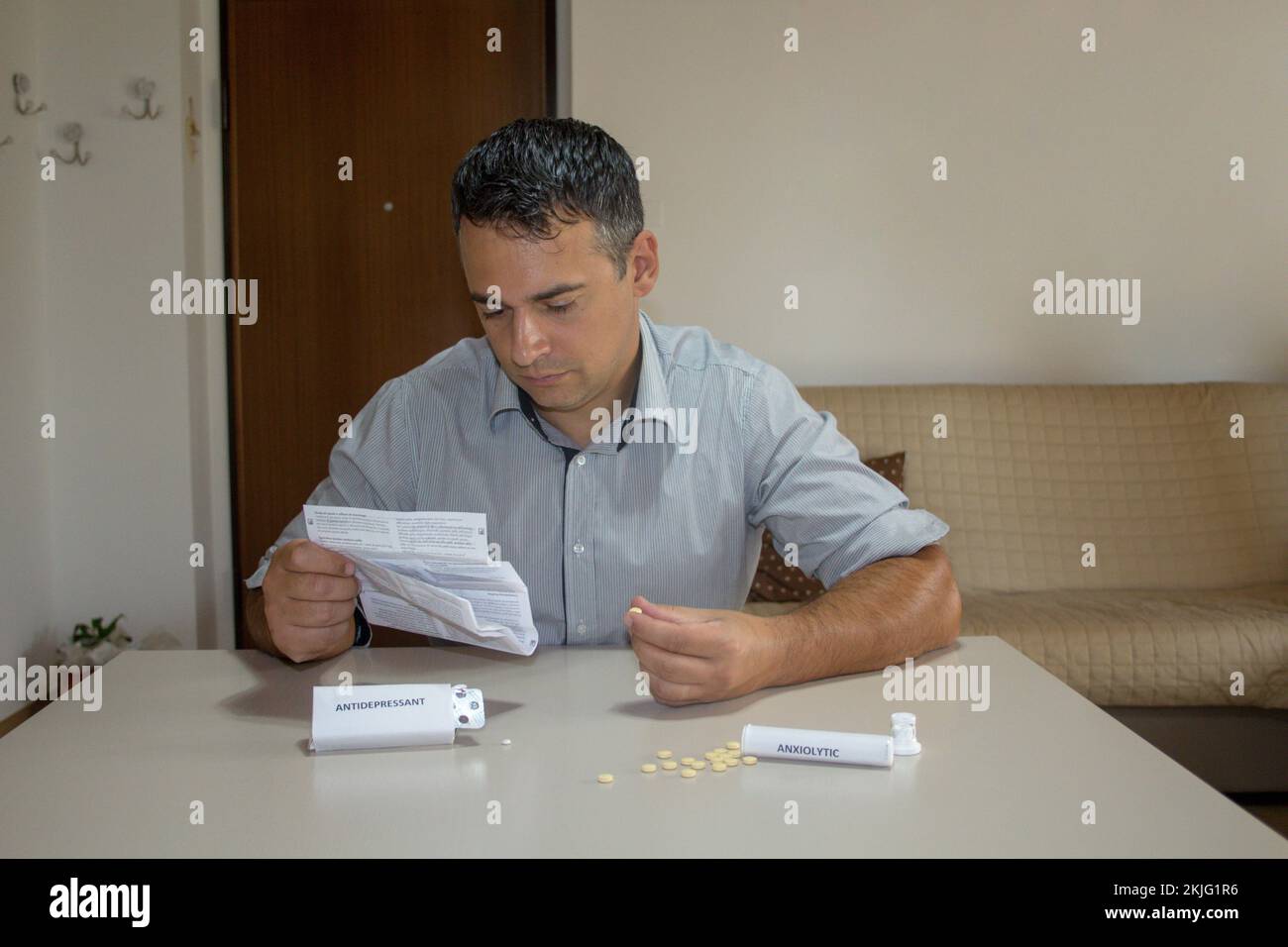 Homme assis en lisant la notice des médicaments avec des pilules anxiolytiques et antidépresseurs dispersées sur la table. Banque D'Images