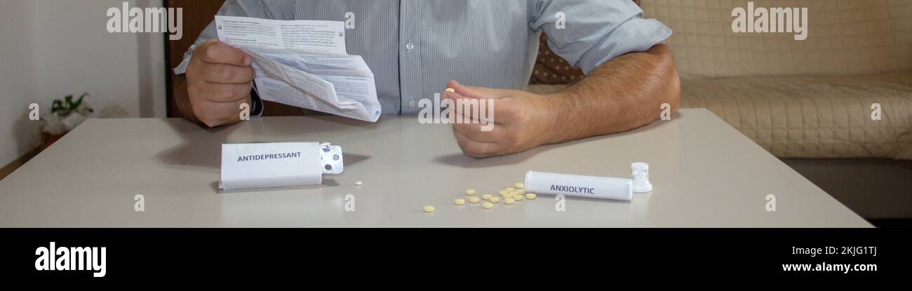 Homme assis en lisant la notice des médicaments avec des pilules anxiolytiques et antidépresseurs dispersées sur la table. Problème et conséquences Banque D'Images