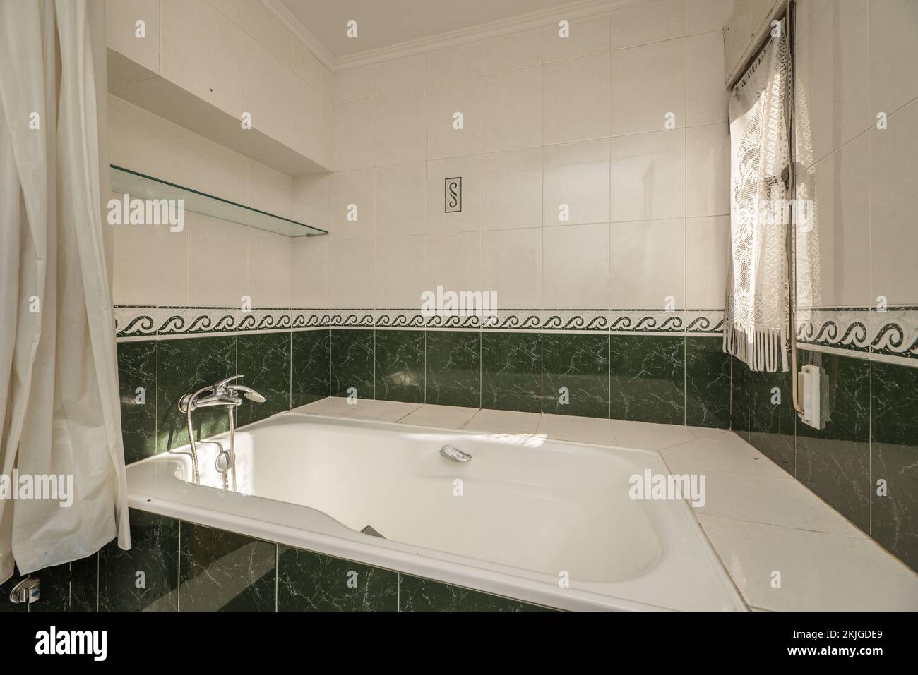 Salle de bains carrelée de vert, baignoire à remous blanche et fenêtre avec rideaux en filet blanc Banque D'Images