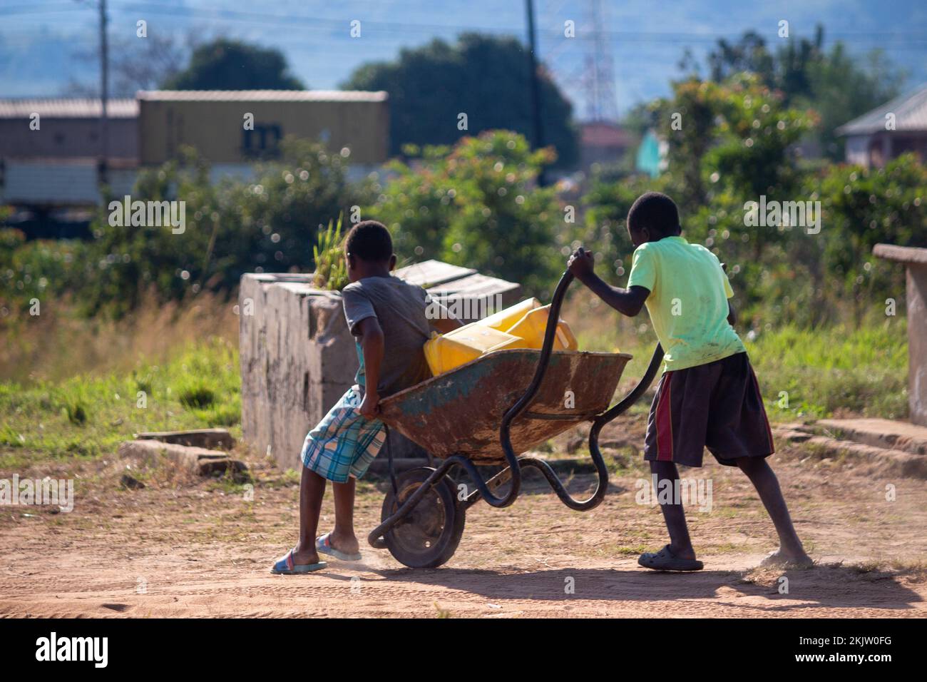 Garçon poussant la brouette avec son frère à l'intérieur sur une route de terre Banque D'Images