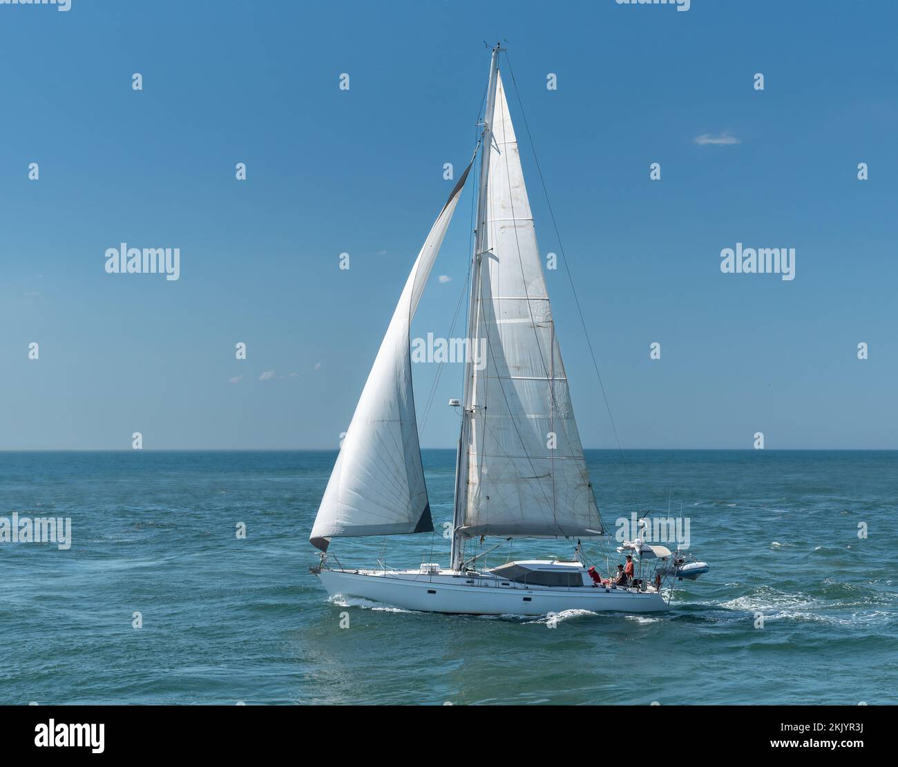 Un yacht blanc sous la voile sur l'océan avec trois personnes non identifiées à bord. Banque D'Images