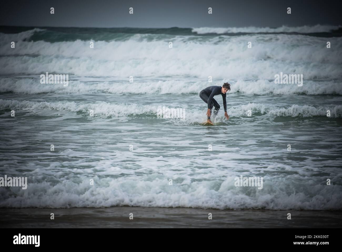 Un surfeur passe les vagues sur les mers accidentées au large de la côte ouest française près de Mimizan, en France Banque D'Images