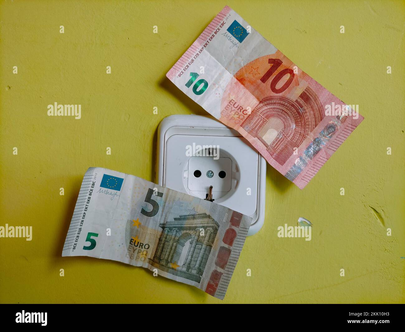Un gros plan des factures d'euros et une prise de courant sur un mur jaune - coût de l'électricité, augmentation des prix de facture d'énergie concept Banque D'Images