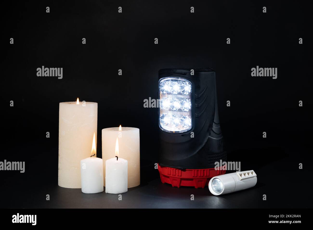 Lampes torches électriques et bougies allumées sur fond noir, sources alternatives de lumière et de chaleur Banque D'Images