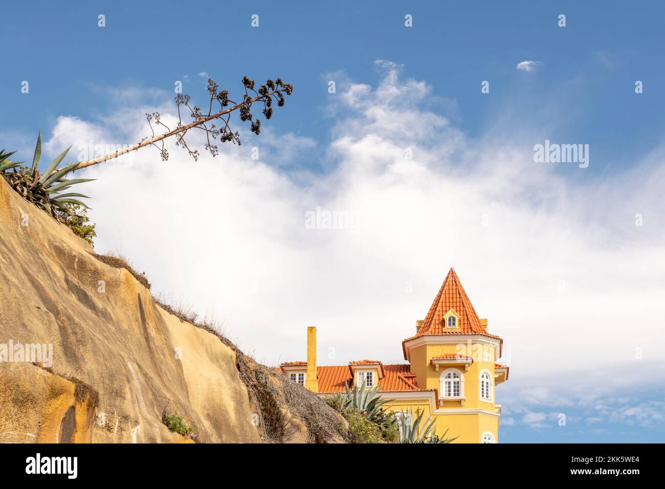 Image d'un bâtiment avec des toits uniques, un ravin avec des aloès et des arbres tombés et de grands nuages blancs dans le ciel Banque D'Images