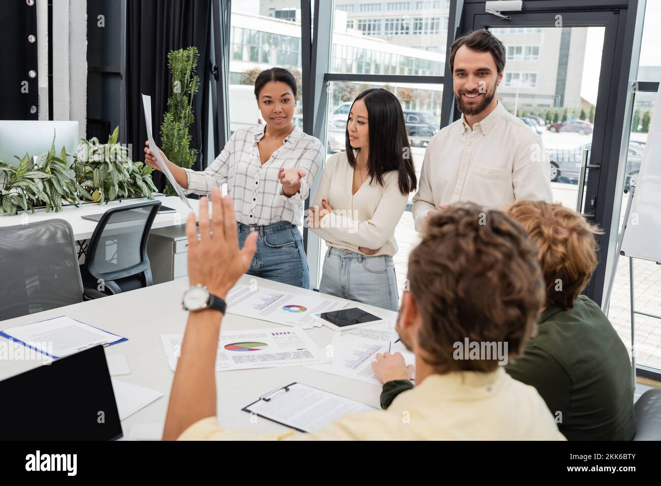 femme multiraciale tenant un document et pointant vers un collègue avec une main levée sur un premier plan flou Banque D'Images