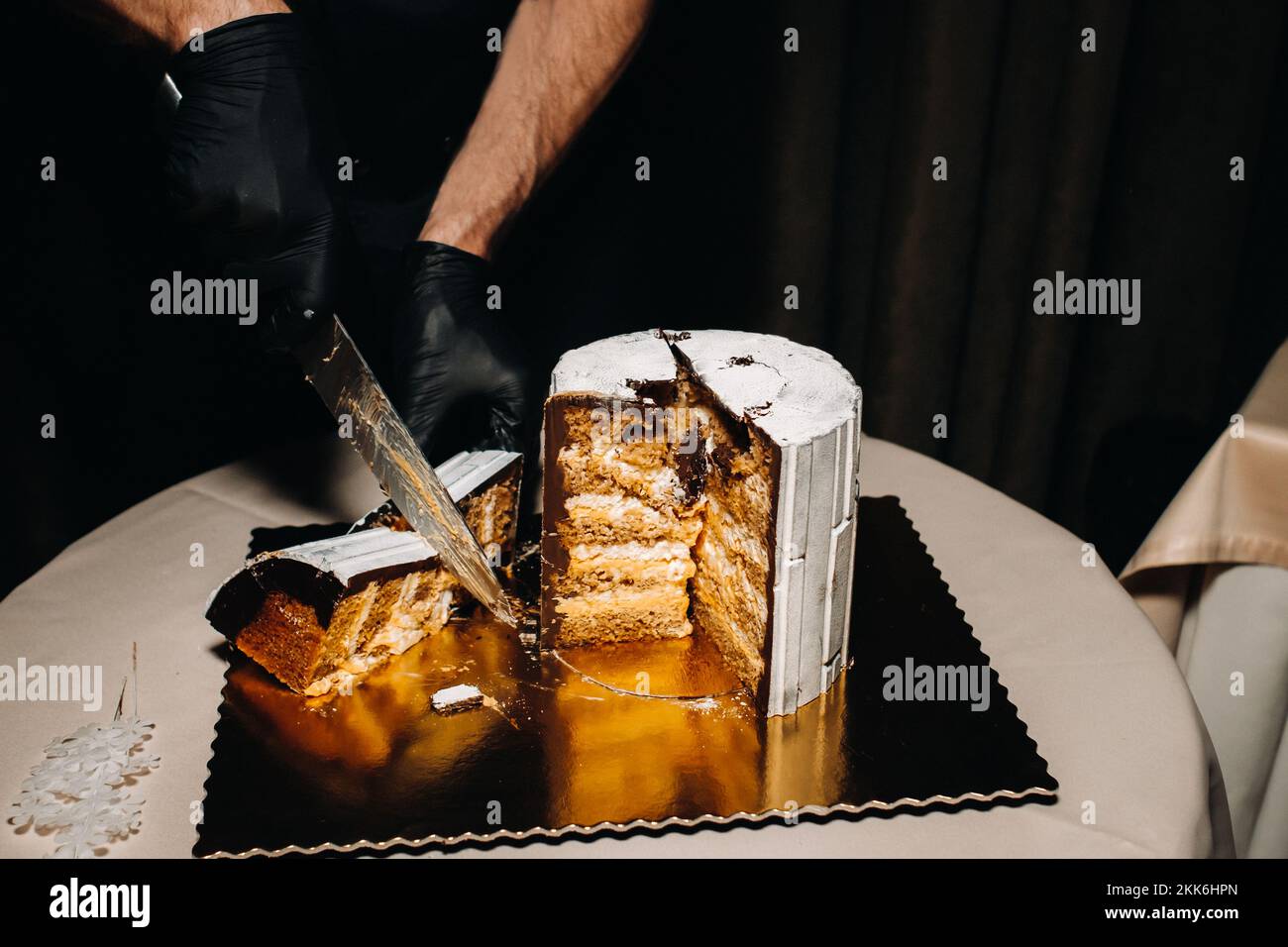 Des gâteaux incroyables. Un chef aux gloved noirs coupe un gâteau de mariage au chocolat. Le gâteau de mariage est délicieux à l'intérieur sur un fond noir.Grand gâteau en blanc Banque D'Images