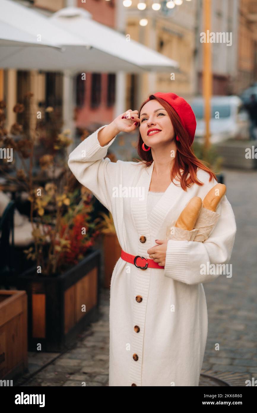 Portrait d'une jolie femme dans un béret rouge et d'un gilet blanc avec des baguettes dans ses mains se balader dans la ville d'automne Banque D'Images