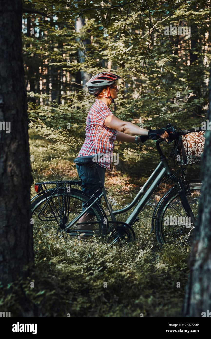 Femme active qui passe des vacances d'été gratuites lors d'un voyage à vélo dans une forêt. Femme portant un casque de vélo et des gants tenant un vélo avec une strophe de panier Banque D'Images