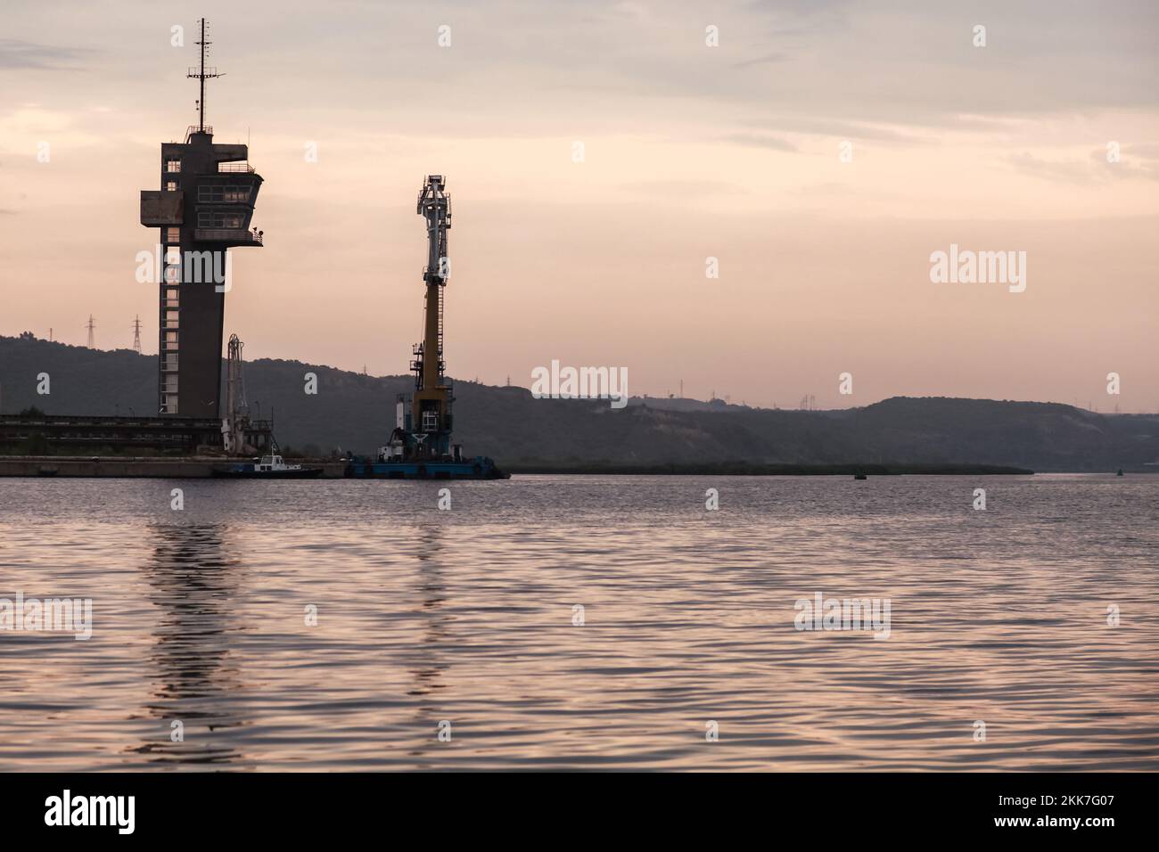 Paysage côtier avec tour de contrôle de la circulation maritime et grue flottante dans la soirée. Port de Varna, Bulgarie. Banque D'Images
