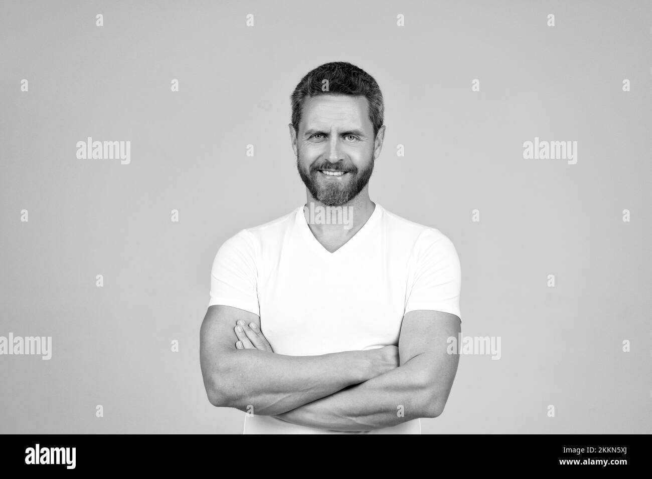 Joyeux homme confiant sourire en gardant les bras croisés dans blanc tshirt fond gris, gars Banque D'Images