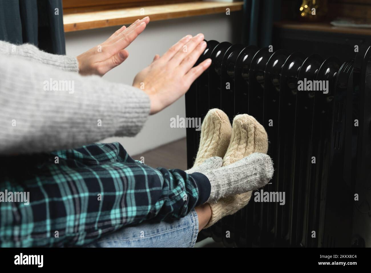 Femmes et enfants assis et se réchauffant les mains et le chauffage électrique. Prix élevés de l'énergie et maison froide. Banque D'Images