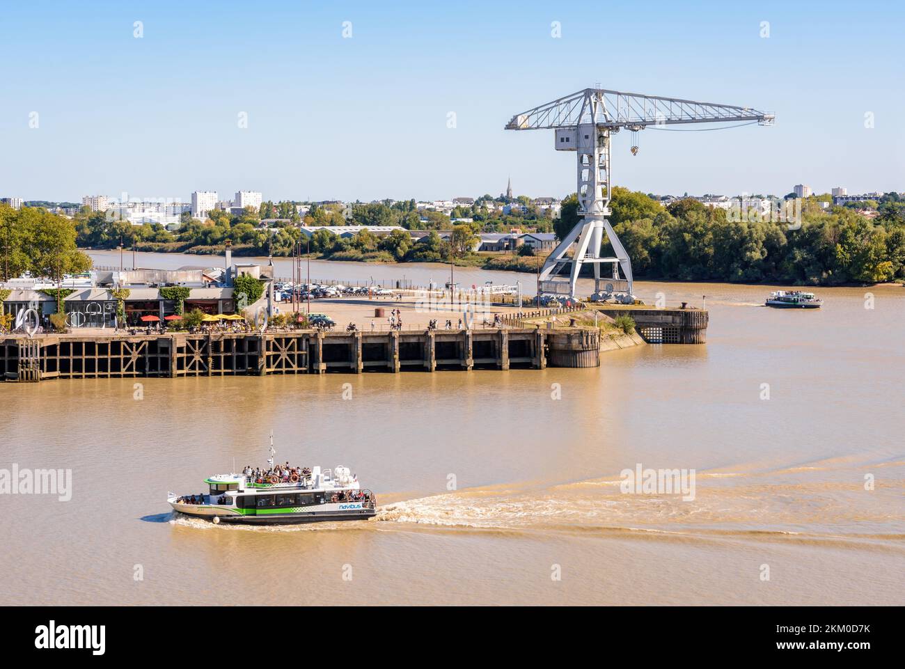 Les bateaux-bus Navibus du réseau de transports publics de Nantes (TAN) naviguent sur la Loire, passant par la grue grise Titan sur l'île de Nantes, en France. Banque D'Images