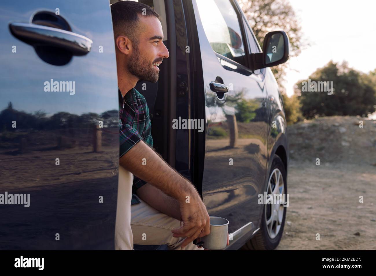 homme souriant à la porte d'une camionnette de camping avec une tasse Banque D'Images