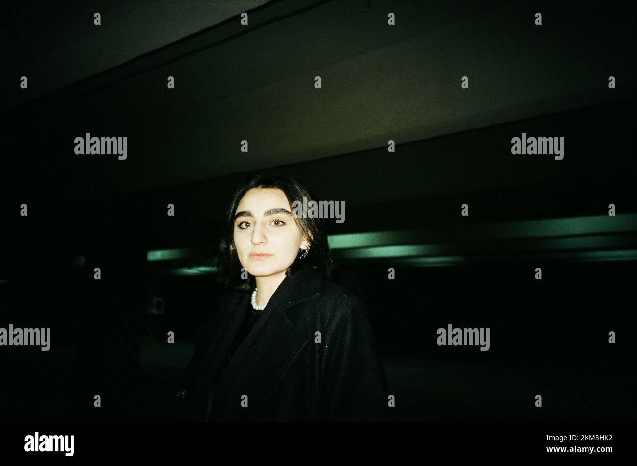 Un portrait d'une belle femme caucasienne aux cheveux courts foncés posé dans un parking souterrain sombre tourné sur film Banque D'Images