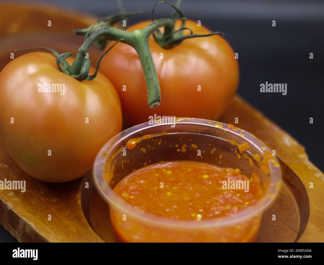 sauce tomate épicée, et tomates dans une platte de bois, fond noir Banque D'Images