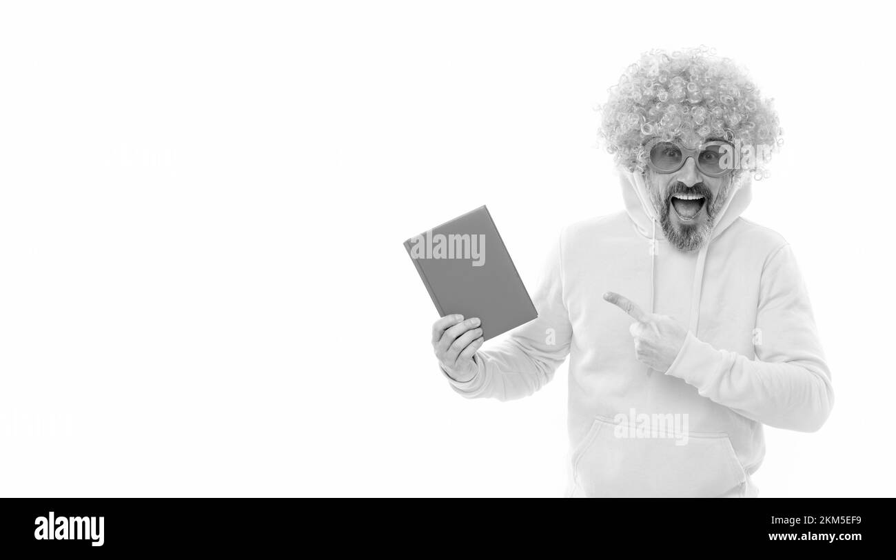 L'enseignant fou de l'école dans la perruque et les lunettes de soleil pointe à la couverture de livre bleu pour l'espace de copie, livre scolaire Banque D'Images