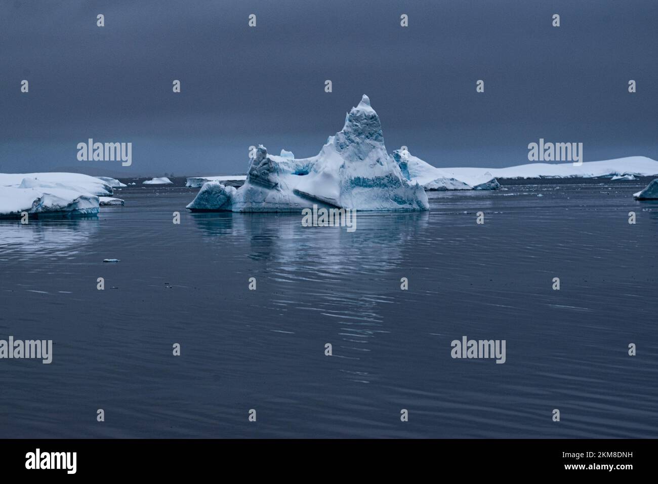 Iceberg et sa réflexion dans l'océan Antarctique calme. Avec des nuages de tempête sombres reflétés dans l'eau. Banque D'Images