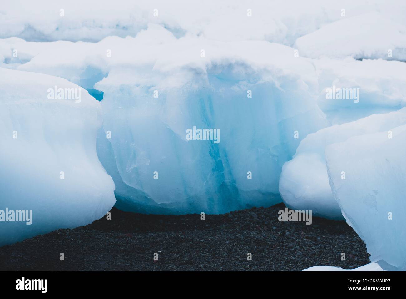 Glaciers blocs bleus de glace et de neige fondent sur la plage de galets noirs en Antarctique. Banque D'Images