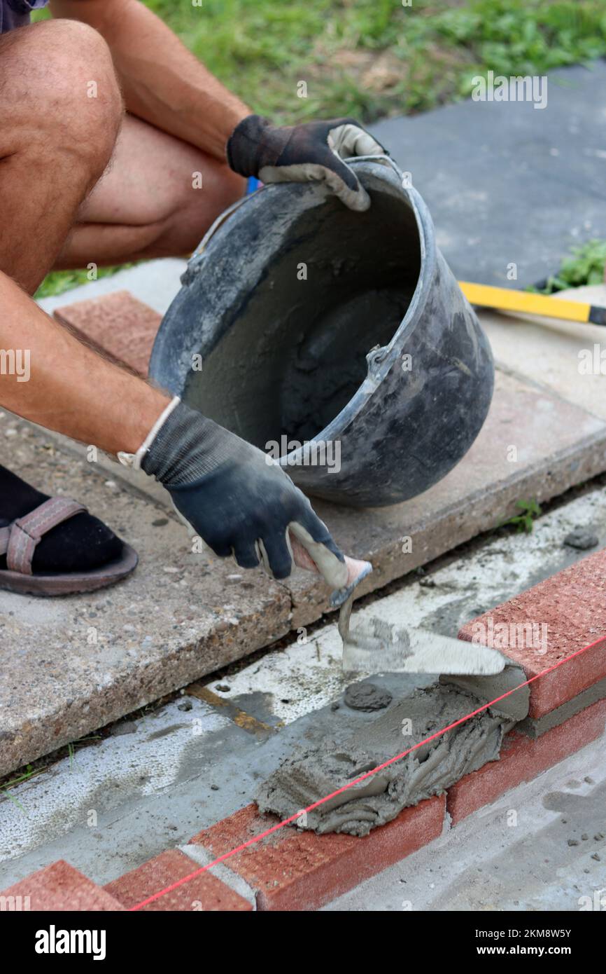 Travaux de construction en cours. Homme constructeur travaillant avec des briques rouges. Photo de près du mur de maçonnerie. Banque D'Images