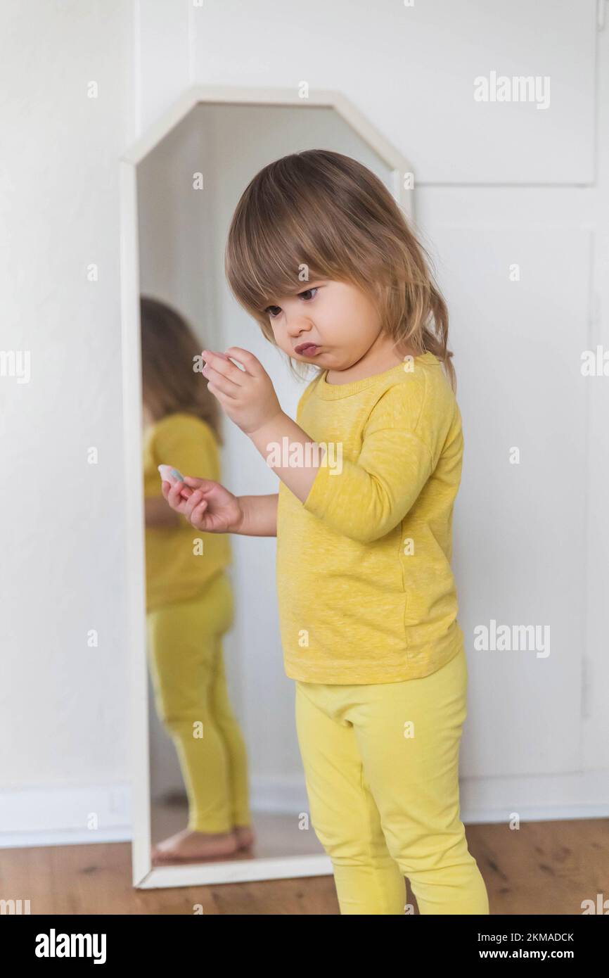 Bébé charmant examine avec scepticisme un peu de trinket près du miroir Banque D'Images