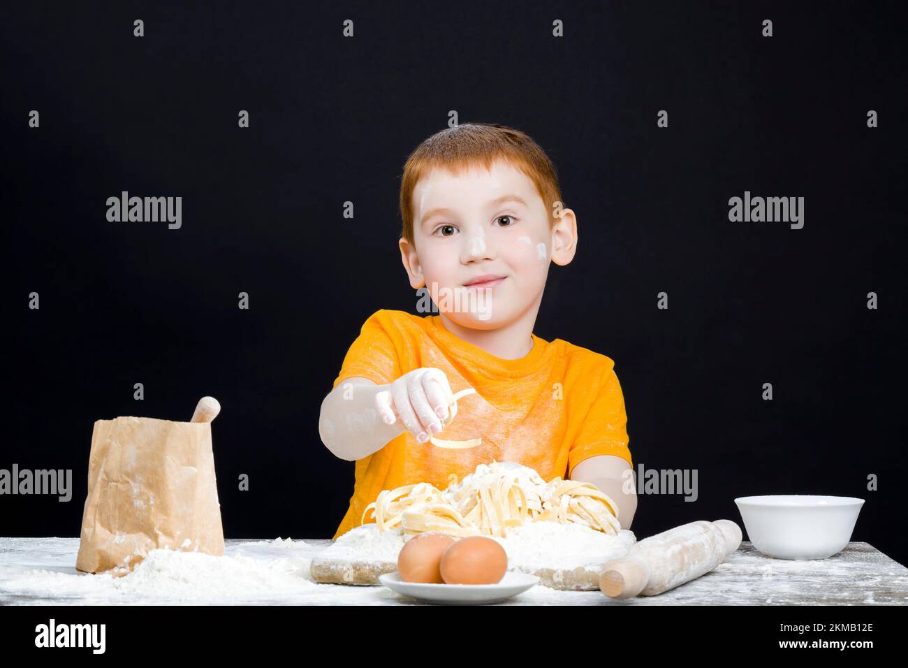 bébé garçon dans la cuisine tout en aidant à préparer la nourriture, garçon avec des cheveux rouges et de belles caractéristiques du visage, bébé jouant avec la farine dans la cuisine Banque D'Images