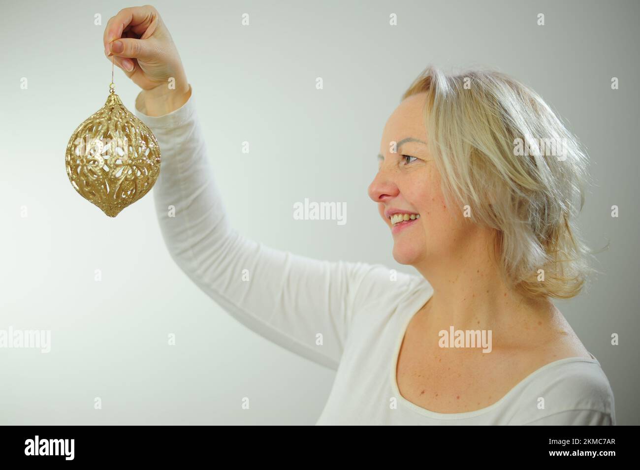 Noël arbre décoration fête invitation adulte femme avec cheveux gris avec un jouet doré du nouvel an dans sa main belle boule dorée brillante Banque D'Images
