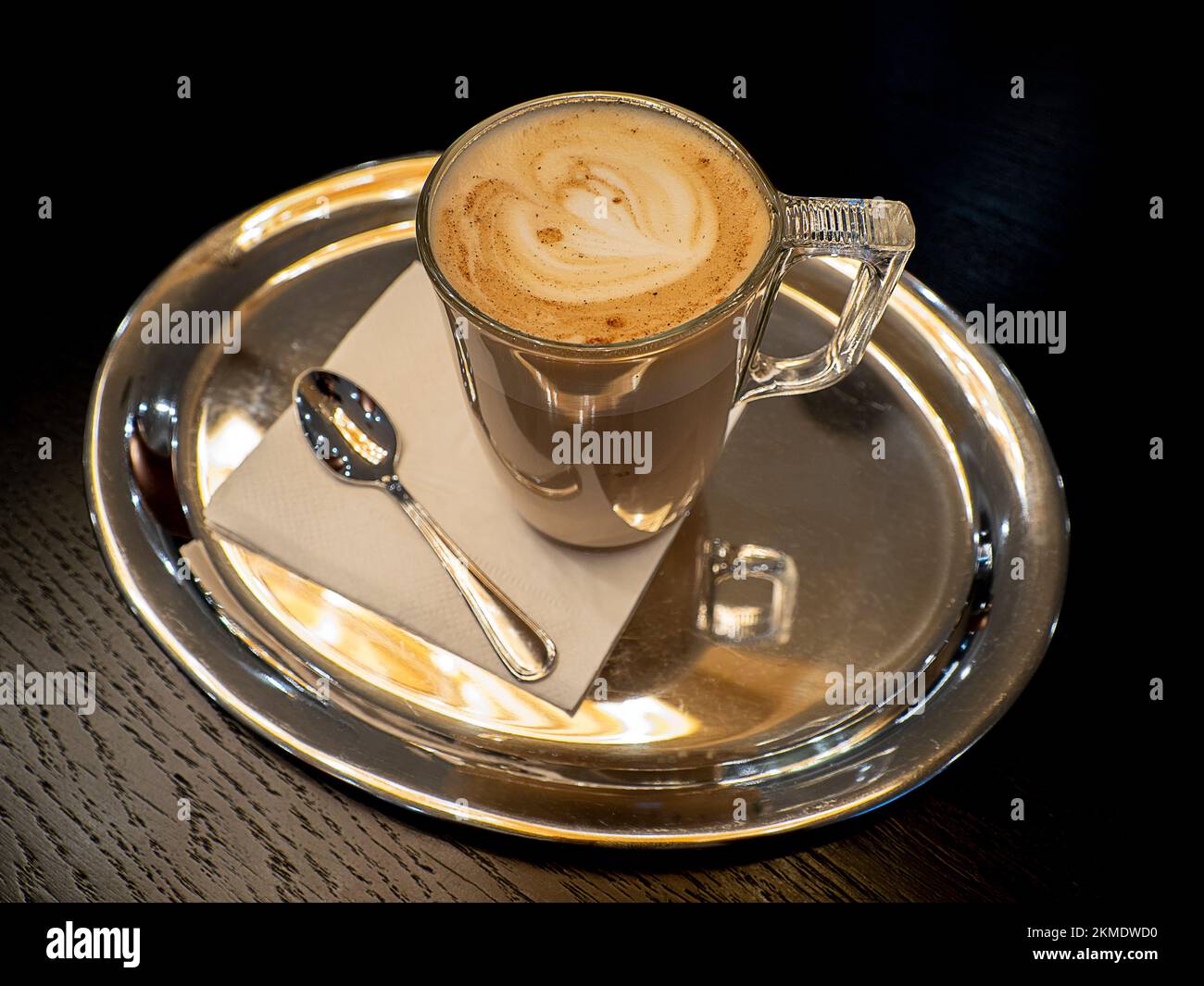 la tasse de café en verre sur la soucoupe metall avec l'art du lait sur la table en bois Banque D'Images