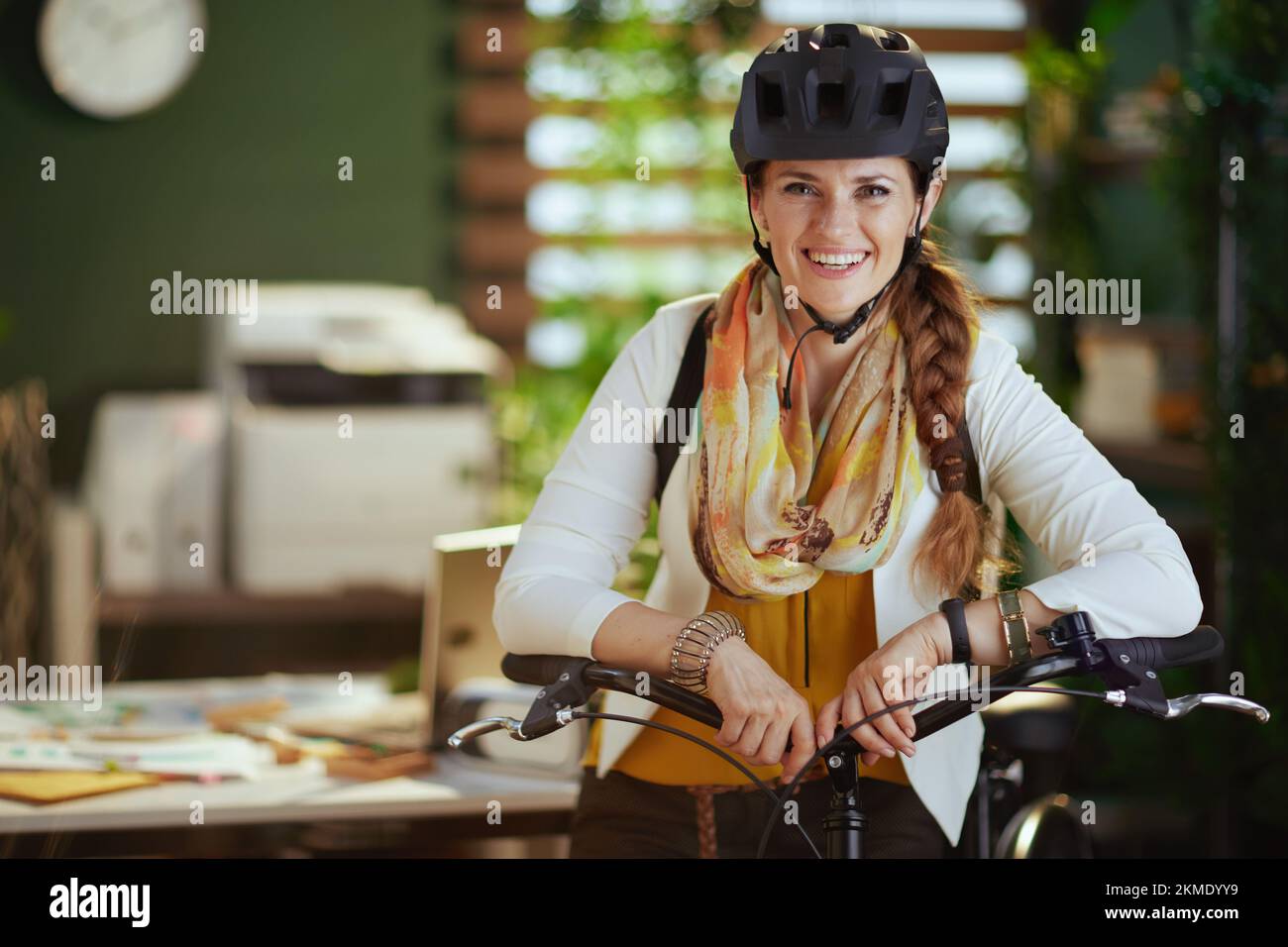 Portrait d'une heureuse femme d'affaires tendance de 40 ans dans un casque  de vélo avec vélo dans un bureau écologique moderne Photo Stock - Alamy