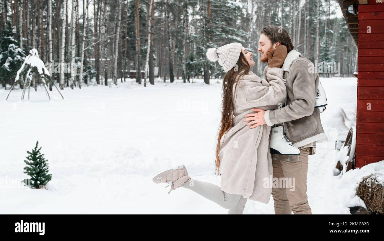 Jeune fille de couple marchant près de la grange avec des patins. Hiver enneigé et froid à la campagne. Patinage, embrasser, s'amuser, rire dans des vêtements élégants, la fourrure Banque D'Images