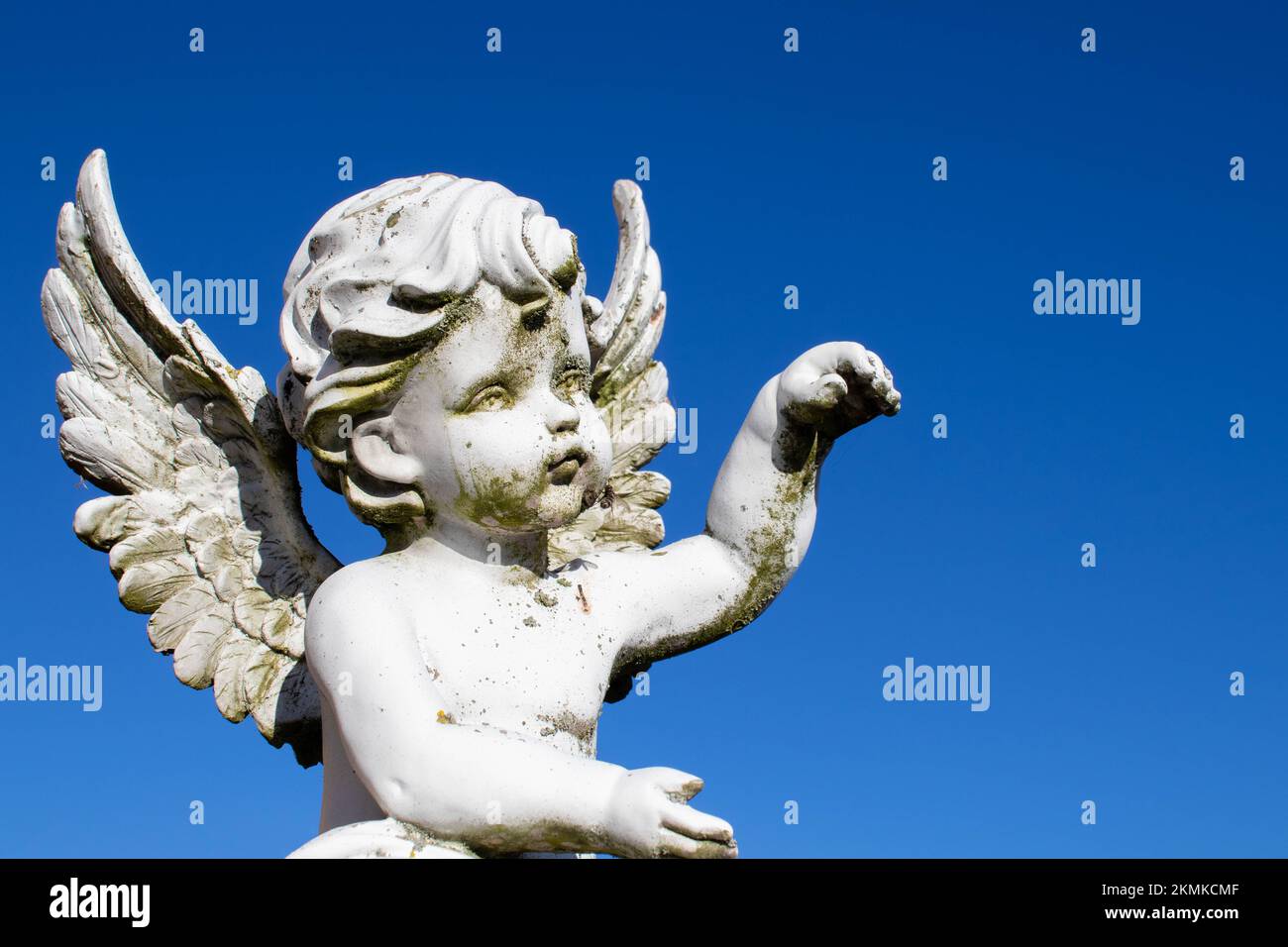 Triste sculpture d'ange gardien avec de longues ailes ouvertes à travers le cadre désaturé contre un ciel blanc brillant. La triste sculpture d'expression avec les yeux vers le bas Banque D'Images